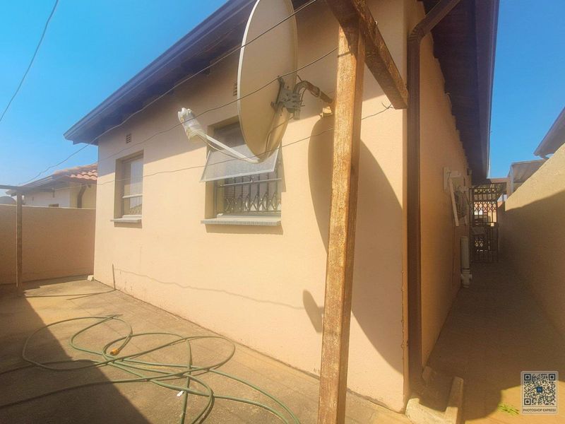 Rear exterior view of the property showing paved area, security bars on windows, and a satellite dish installation.
