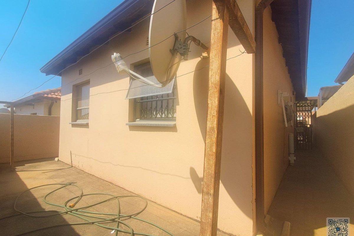 Rear exterior view of the property showing paved area, security bars on windows, and a satellite dish installation.