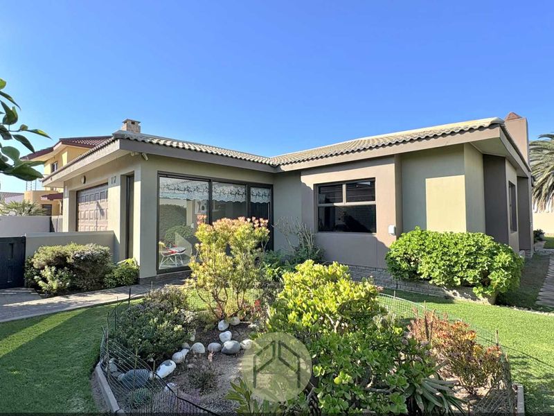 A well-maintained single-story house featuring a tiled roof, paved driveway, integrated garage, and a landscaped front garden with a stone pathway.