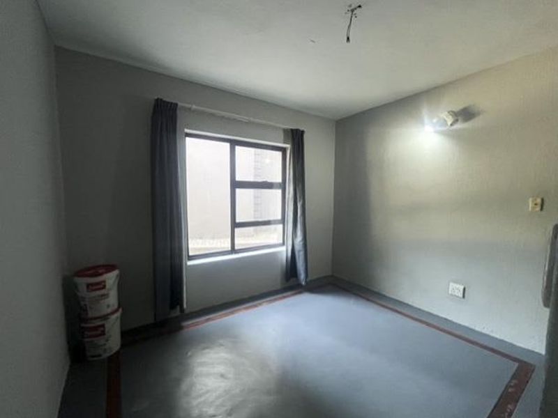 An empty bedroom featuring a large aluminium window, painted concrete flooring, and wall-mounted lighting, ready for renovation or custom interior design.