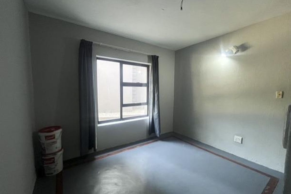 An empty bedroom featuring a large aluminium window, painted concrete flooring, and wall-mounted lighting, ready for renovation or custom interior design.