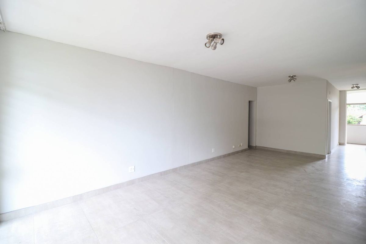 A bright, spacious, and empty living area featuring neutral tiled flooring and modern ceiling spotlights, offering a clean canvas for interior design.