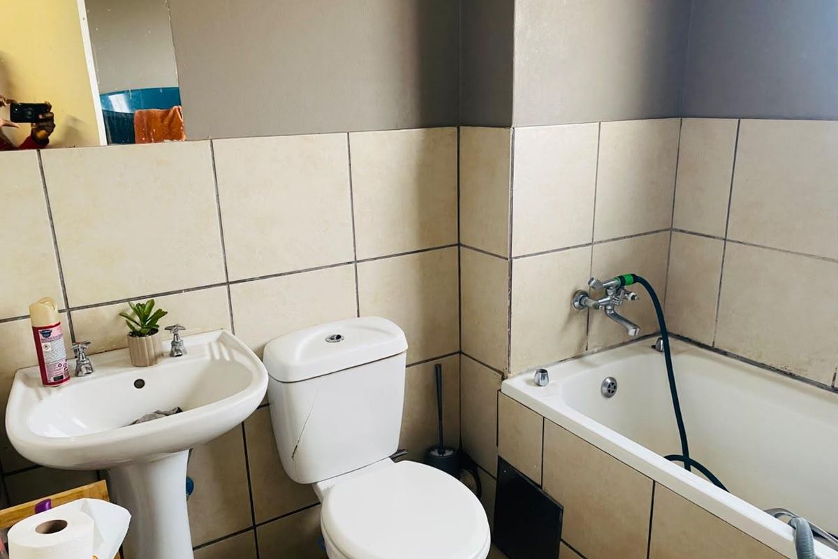A functional bathroom featuring a pedestal basin, toilet, and bathtub with tiled walls. The space shows signs of wear and requires maintenance.