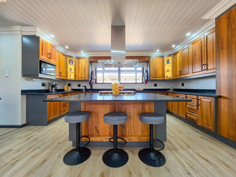 Modern kitchen featuring extensive wooden cabinetry, a central island with stone countertops, integrated appliances, and stylish recessed lighting under a tongue and groove ceiling.