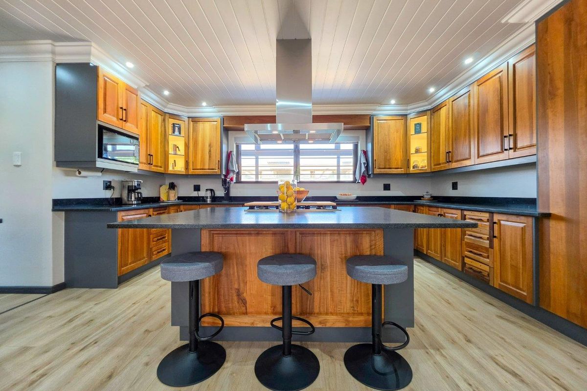 Modern kitchen featuring extensive wooden cabinetry, a central island with stone countertops, integrated appliances, and stylish recessed lighting under a tongue and groove ceiling.