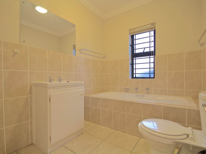 A functional bathroom featuring a built-in vanity, bathtub, toilet, and neutral tiled finishes, offering a clean and practical space.