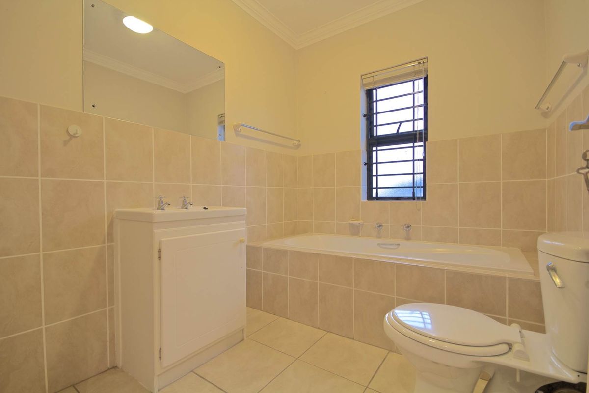 A functional bathroom featuring a built-in vanity, bathtub, toilet, and neutral tiled finishes, offering a clean and practical space.