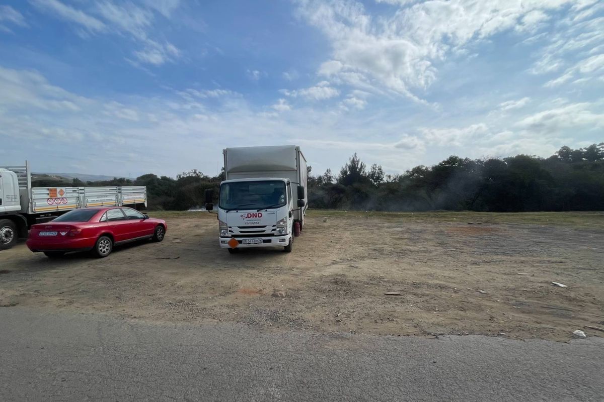 An open, undeveloped commercial land plot with a gravel surface, currently used for vehicle parking.