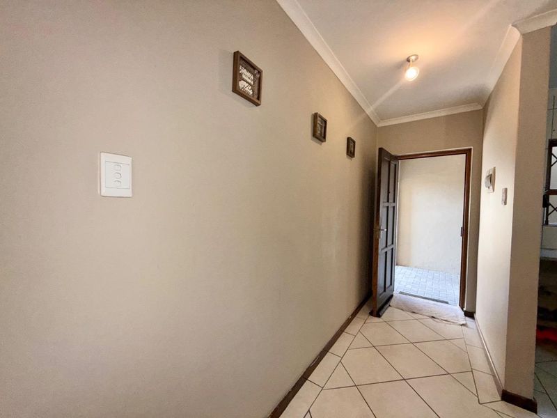 A neutral-toned hallway featuring tiled flooring and a coved ceiling, providing a clean transition space within the townhouse.