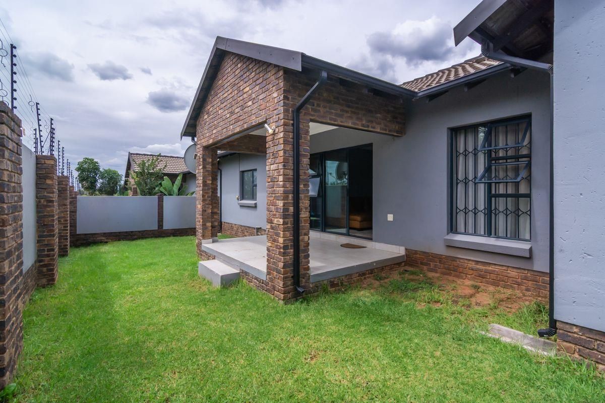 A rear view of the townhouse featuring a covered patio, brick facade, and a private garden area with perimeter security fencing.