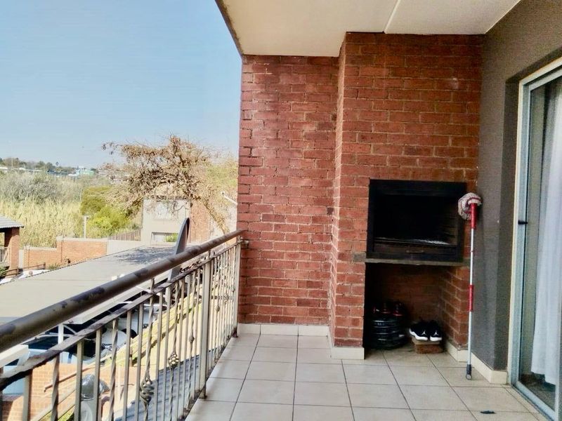 A covered balcony featuring a built-in brick braai, tiled flooring, and a metal balustrade, offering an outdoor space for relaxation and entertaining.