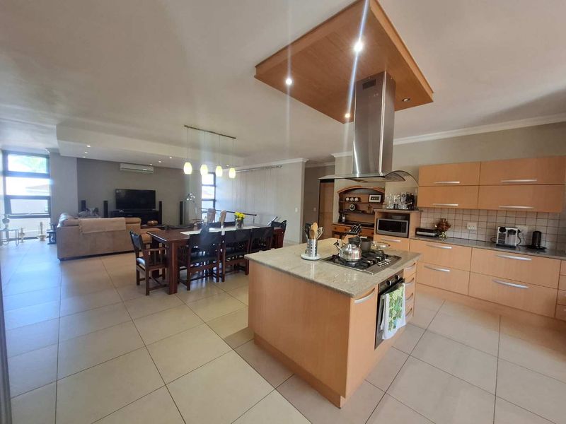 Spacious open-plan living area featuring a modern kitchen with a central island, gas hob, and integrated cabinetry flowing into the dining and lounge space.