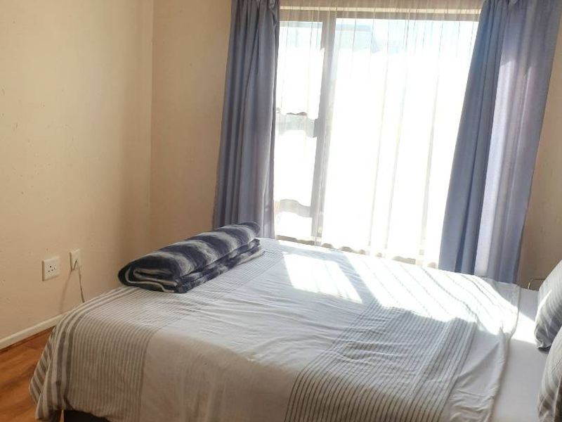 A bedroom featuring laminate wood flooring and a large window with curtain tracks, providing natural light.