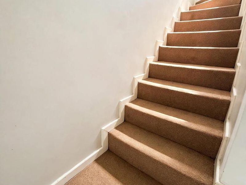 A clean, carpeted staircase leading to an upper level, featuring neutral walls and white skirting boards.
