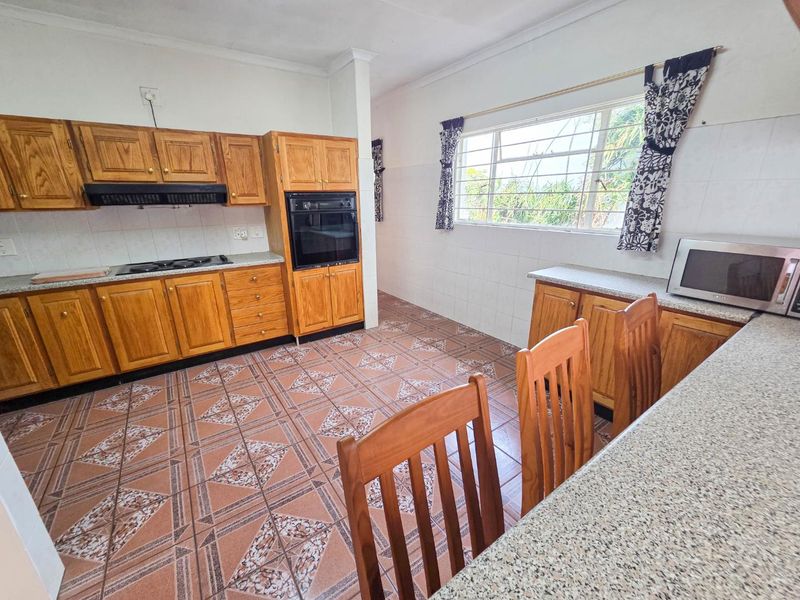 A functional kitchen featuring wooden cabinetry, built-in oven, gas hob, and granite countertops with tiled flooring and splashbacks.