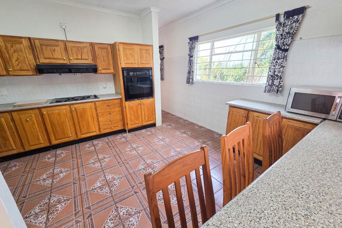 A functional kitchen featuring wooden cabinetry, built-in oven, gas hob, and granite countertops with tiled flooring and splashbacks.
