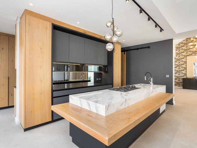 Modern kitchen featuring a large marble-topped island with integrated gas cooktop, sleek dark cabinetry, wood accents, and high-end finishes.