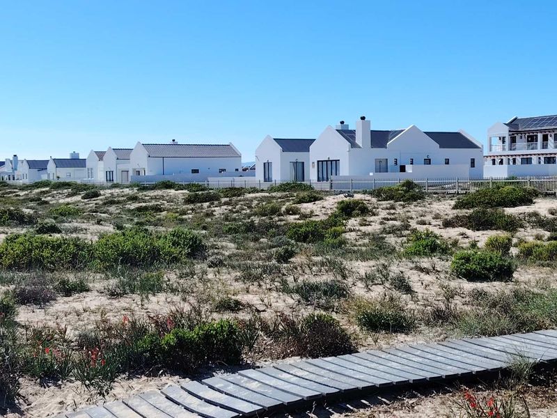 A view of the rear elevations of residential properties featuring white facades and chimneys, with a wooden boardwalk leading through the coastal landscape.