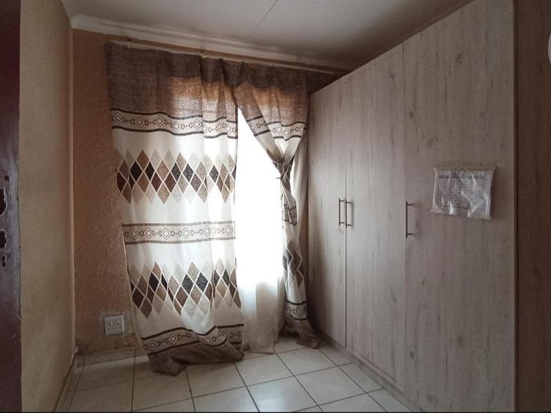 A bedroom featuring tiled flooring and a built-in wardrobe, showing signs of wear on the wall surfaces.