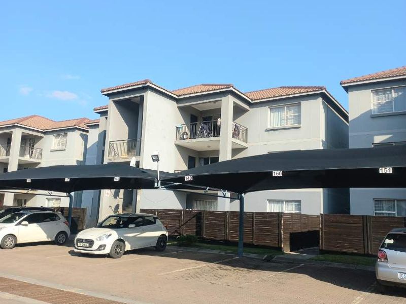 Exterior view of an apartment complex featuring designated shaded parking bays, paved driveway, and multi-story residential units with balconies.