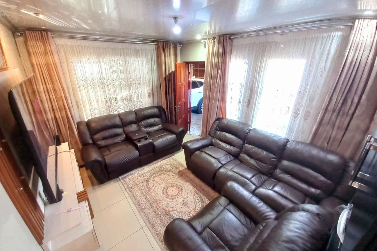 A comfortable living room featuring tiled flooring, large windows with curtains, and direct access to an adjacent area.