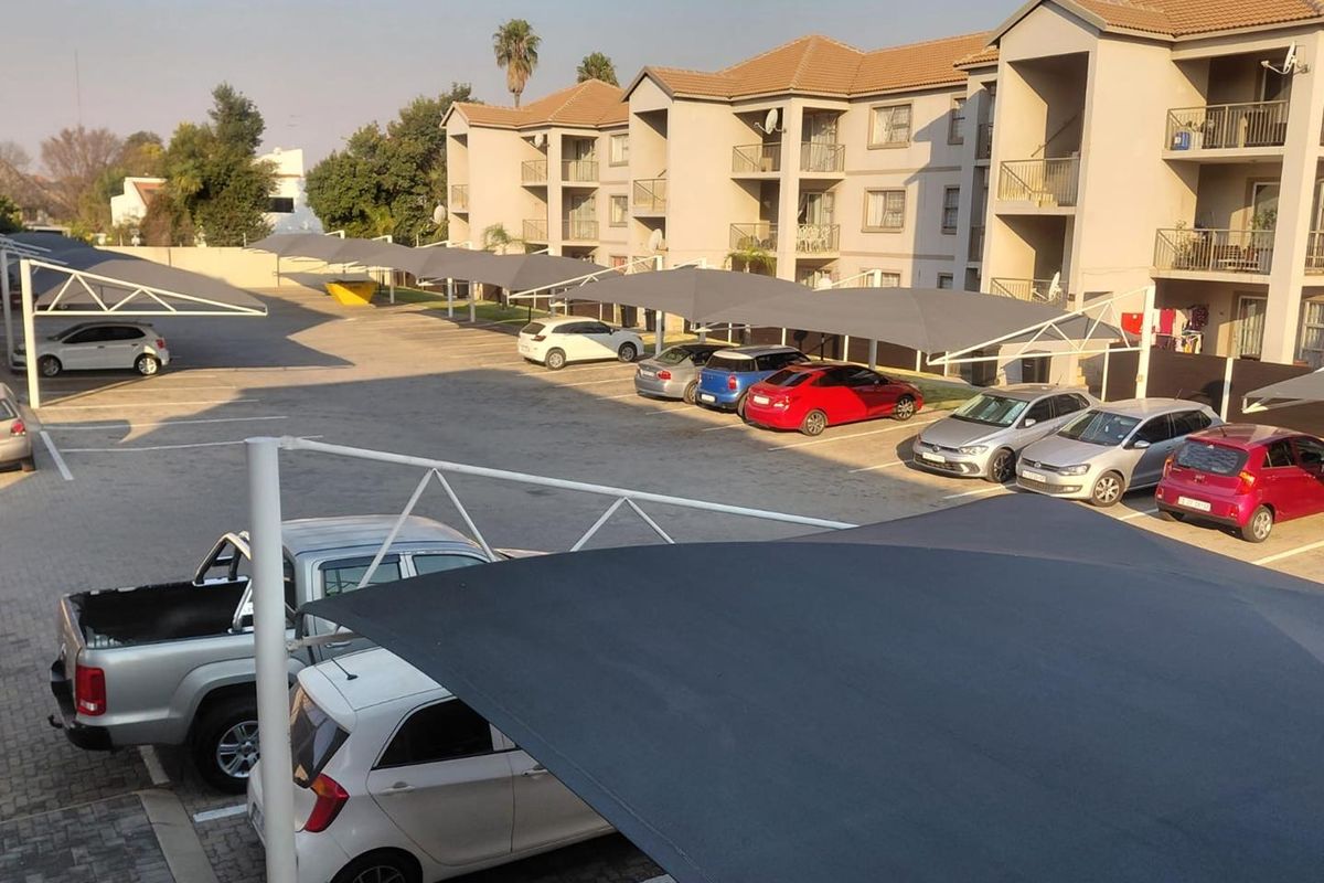 View of the apartment complex parking area featuring structured shade cloth carports and paved parking bays.