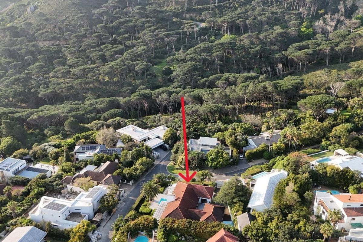 Aerial view of a residential property featuring a tiled roof, private swimming pool, and lush garden setting within a wooded neighborhood.