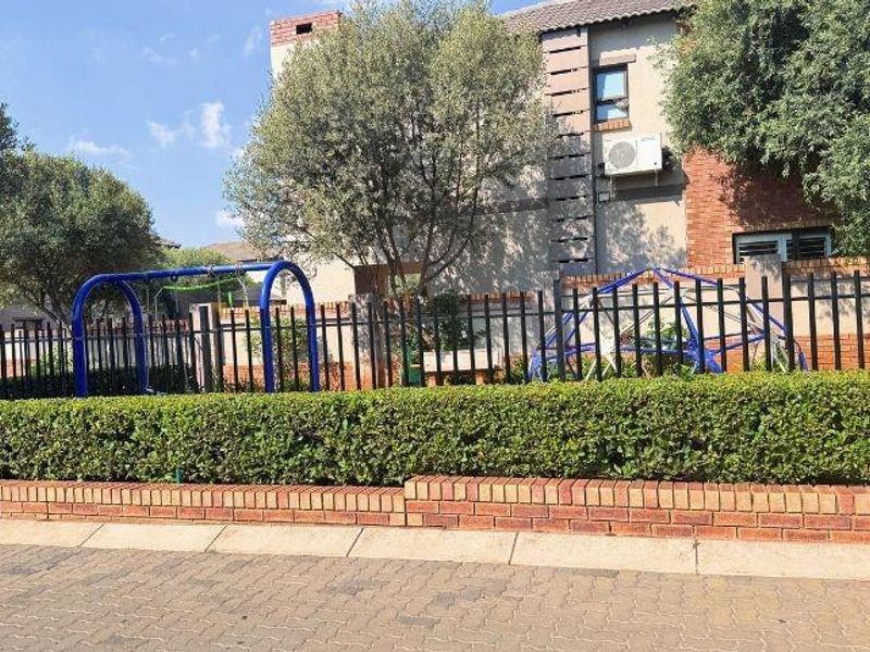 Front exterior view of a townhouse featuring a brick boundary wall, metal security fencing, and established garden hedging.