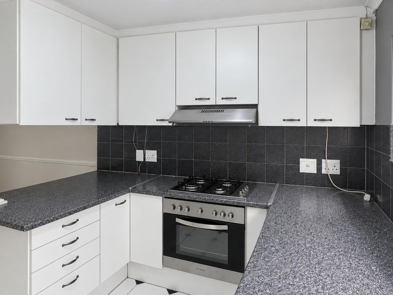 A functional kitchen featuring white cabinetry, dark granite countertops, a gas hob, built-in oven, and a tiled backsplash.