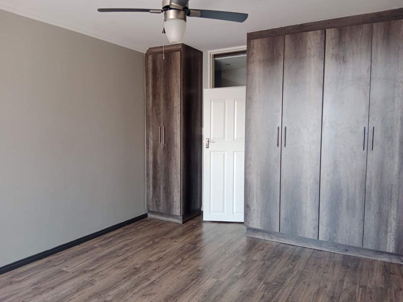 A clean, empty bedroom featuring modern dark wood-look built-in cupboards, laminate flooring, and a ceiling fan.