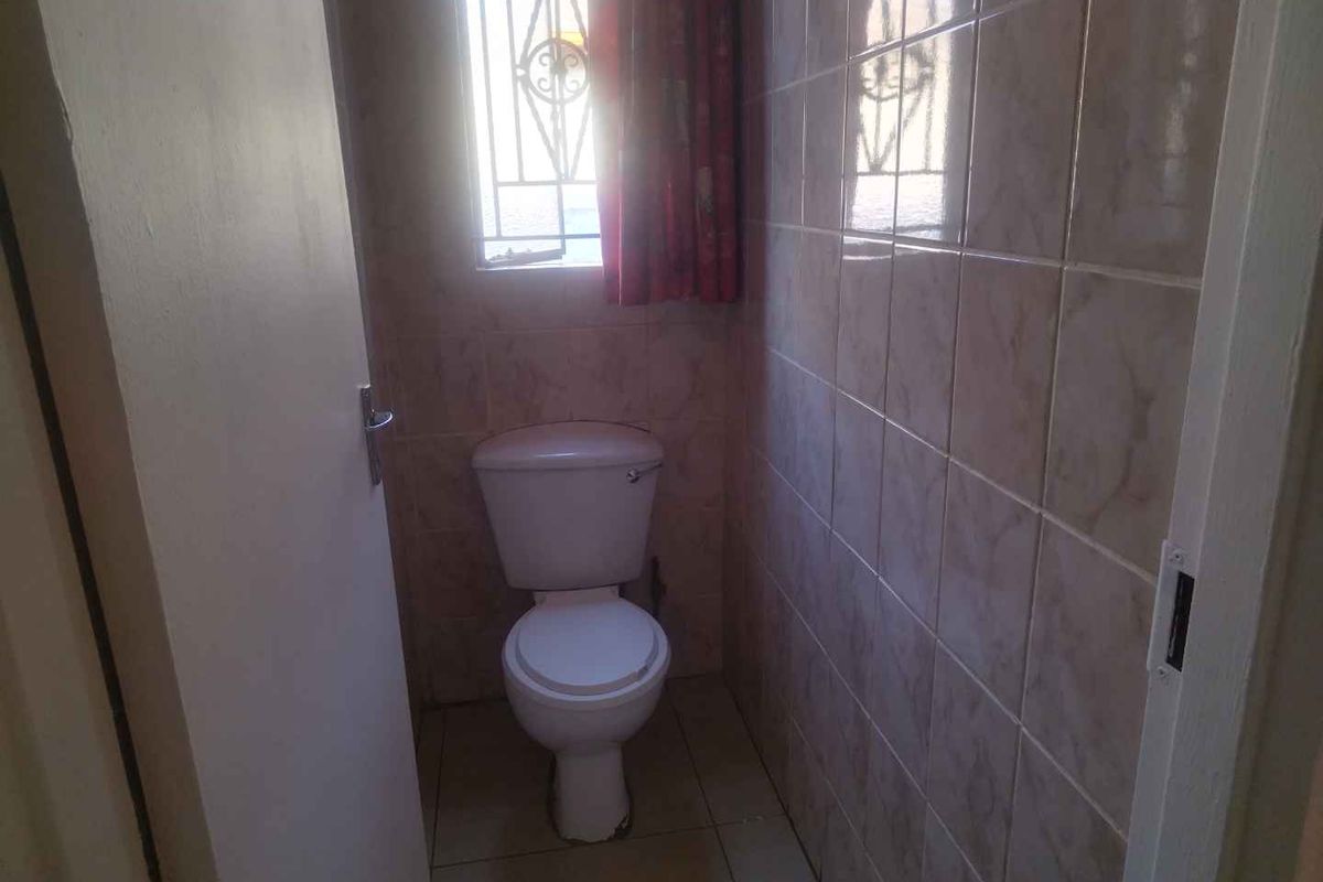 A compact, functional bathroom featuring a standard toilet, tiled walls, and a window with security bars.