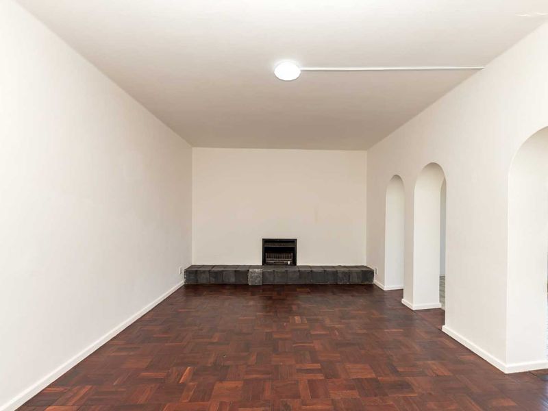 Spacious living room featuring classic parquet flooring, a built-in fireplace with a stone hearth, and elegant arched architectural details leading to an outdoor area.