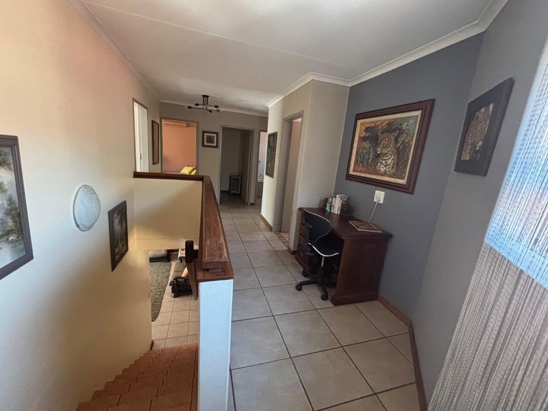 A spacious upper-level hallway featuring tiled flooring, a wooden staircase handrail, and access to multiple rooms.