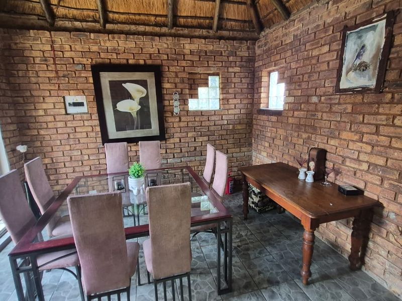A rustic enclosed patio featuring exposed brick walls, a traditional thatched roof, and tiled flooring, providing a cozy space for dining and entertaining.