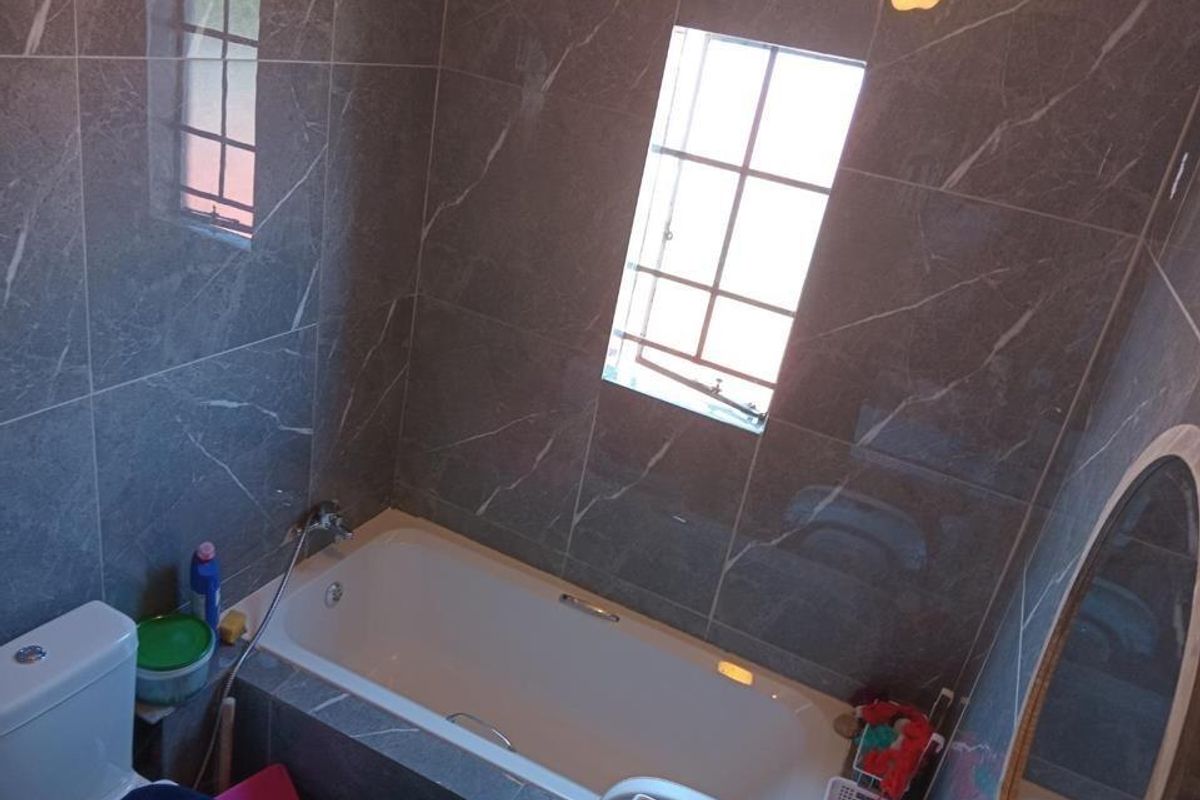 Modern bathroom featuring floor-to-ceiling grey marble-look wall tiles, a built-in bathtub with shower mixer, and a window for natural light.