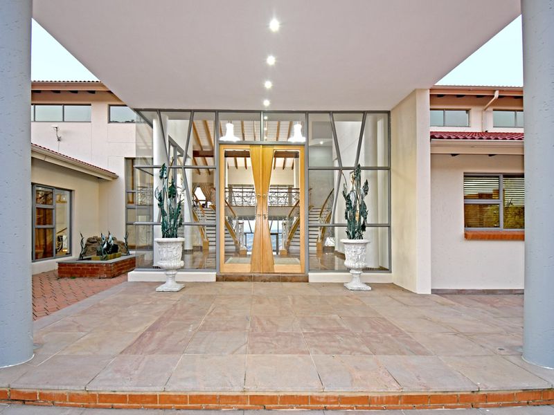 Grand front entrance featuring a covered portico, large glass facade, double timber doors, and tiled patio area with structural columns.