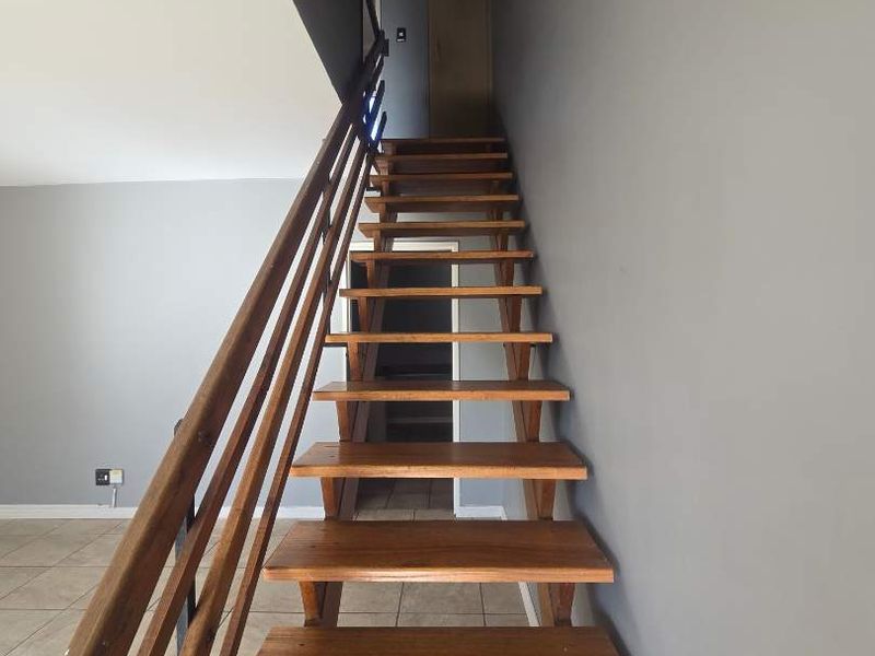 A staircase featuring wooden treads and a matching timber handrail, leading to the upper level of the townhouse.