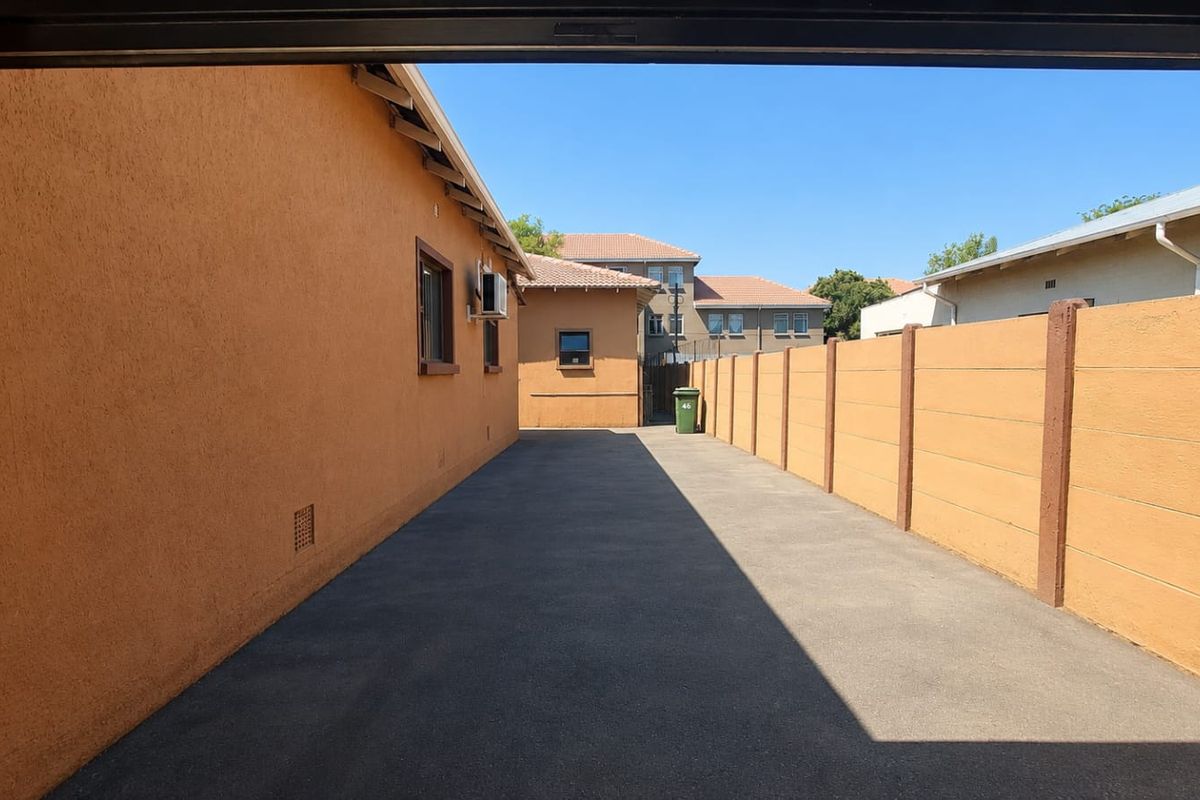 A clean, paved side driveway area featuring a secure precast concrete boundary wall and exterior stucco finish.