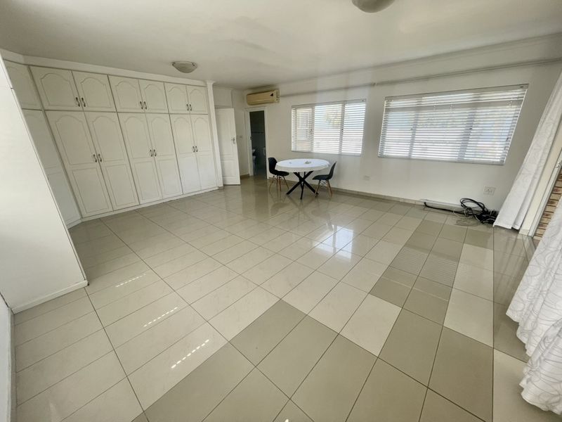 Spacious living area featuring large format tiled flooring, extensive built-in storage cupboards, and wall-mounted air conditioning.