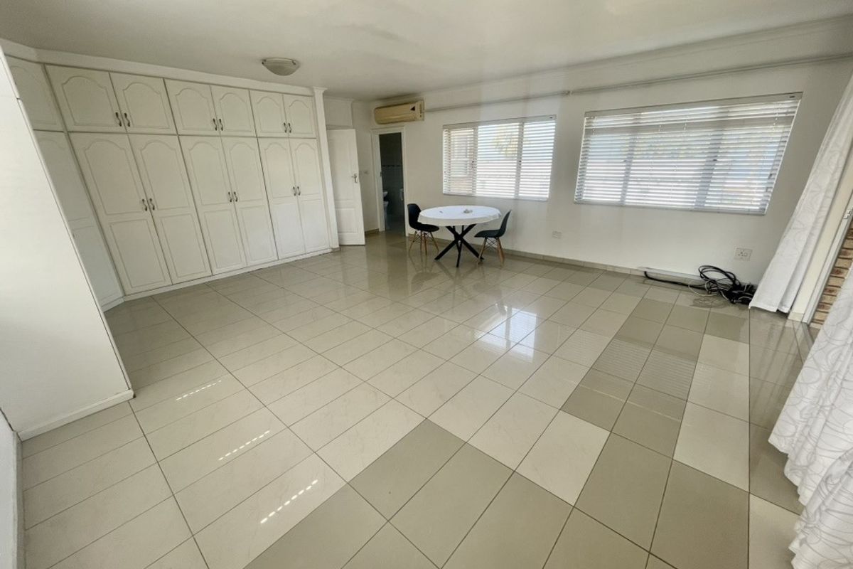 Spacious living area featuring large format tiled flooring, extensive built-in storage cupboards, and wall-mounted air conditioning.