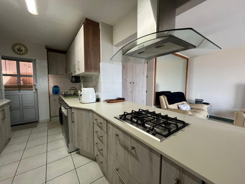 A functional kitchen featuring light wood-grain cabinetry, a gas hob with an overhead extractor fan, and tiled flooring.