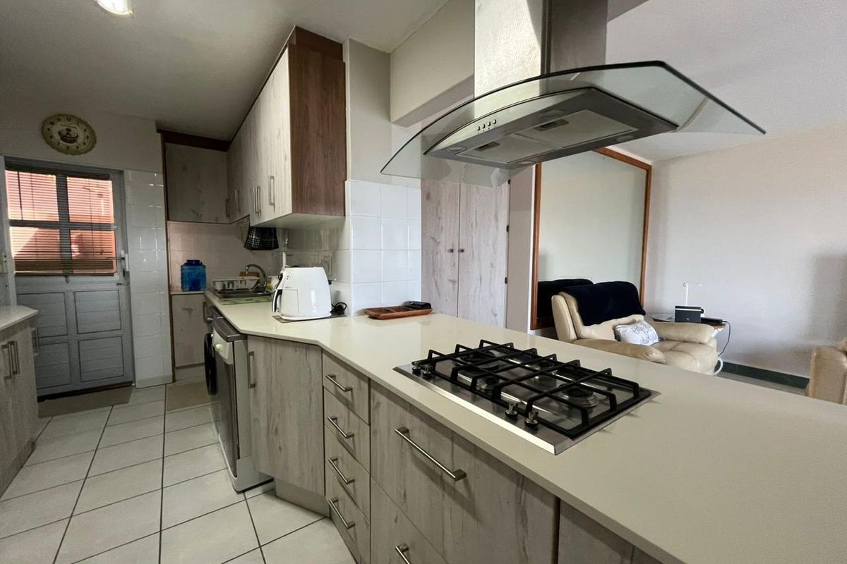 A functional kitchen featuring light wood-grain cabinetry, a gas hob with an overhead extractor fan, and tiled flooring.