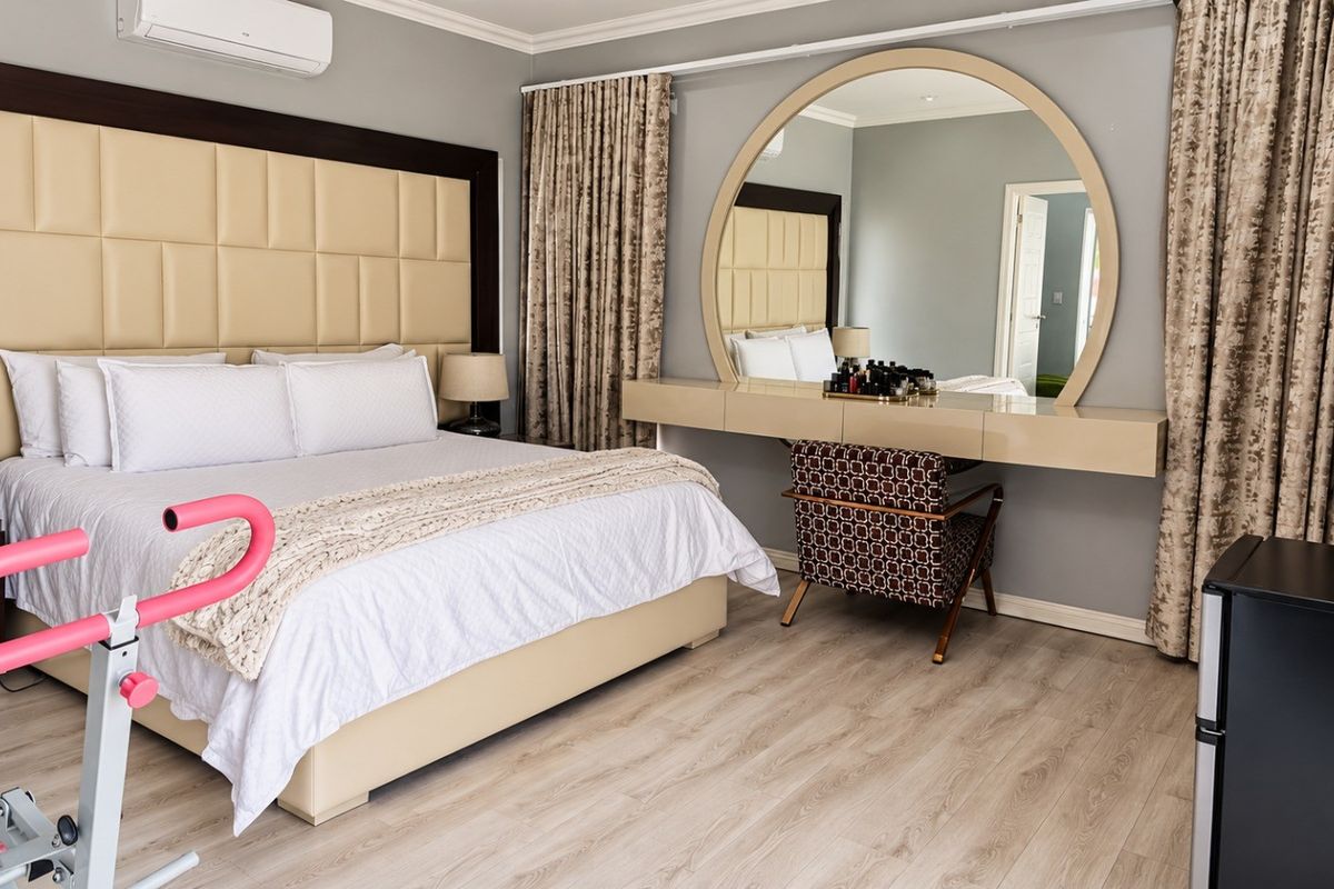 Spacious bedroom featuring laminate flooring, a built-in vanity with a large circular mirror, and a wall-mounted air conditioning unit.