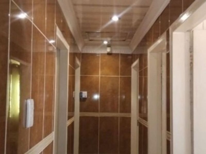 A hallway featuring full-height brown wall tiling and recessed ceiling lighting, providing access to multiple rooms.