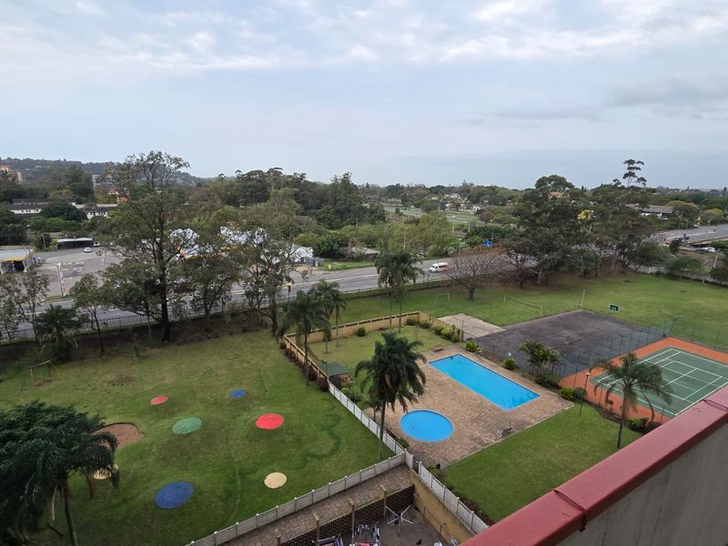 Elevated view overlooking the apartment complex grounds, featuring a swimming pool, tennis court, and landscaped garden areas.