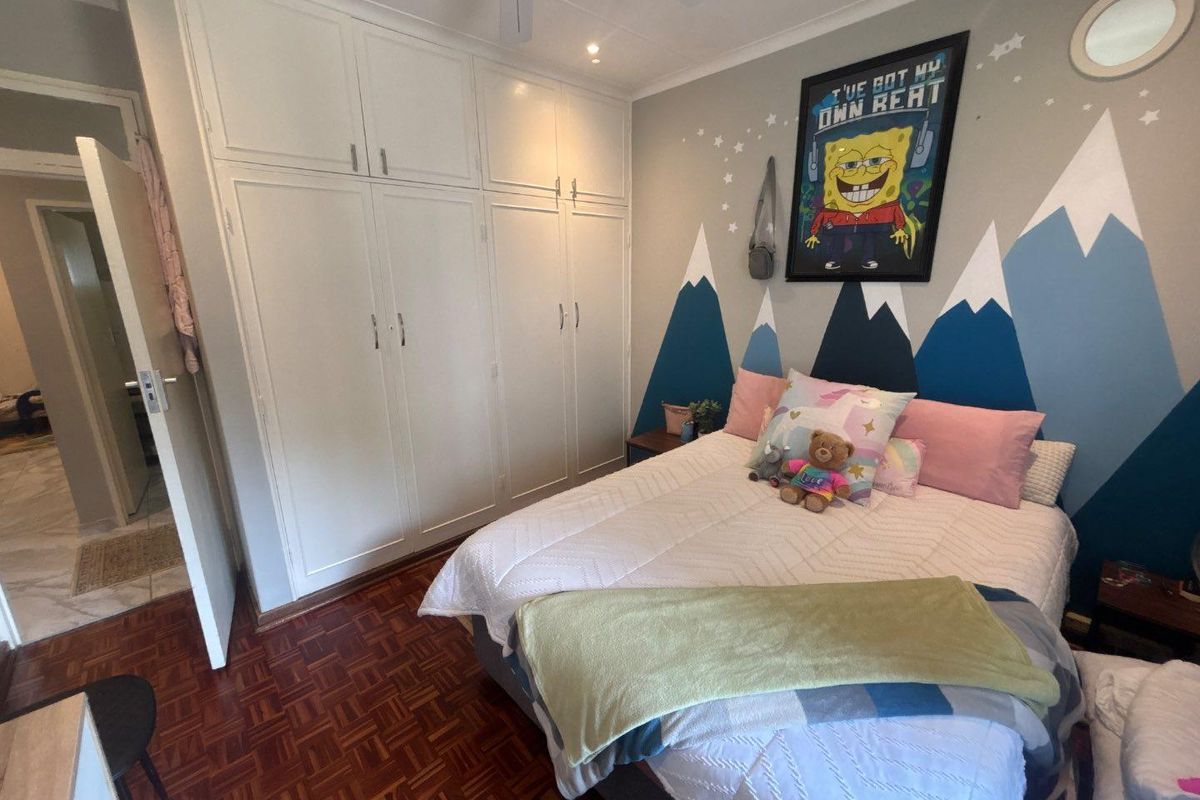 A bedroom featuring classic parquet flooring, ample built-in cupboard storage, and a ceiling fan, offering a functional and well-maintained living space.