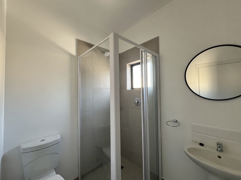 A clean and functional bathroom featuring a corner shower enclosure, pedestal basin, and toilet with neutral wall tiling.