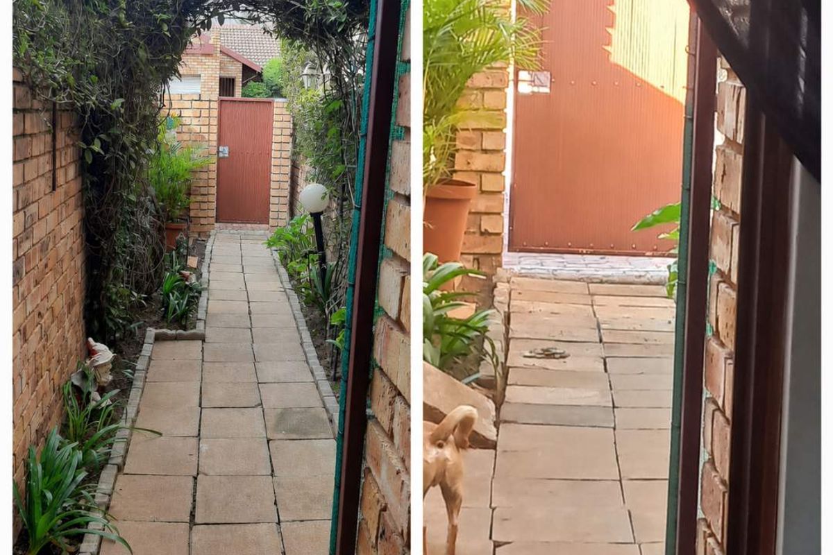 A narrow rear garden pathway featuring brick boundary walls, paved flooring, and a metal gate entrance.