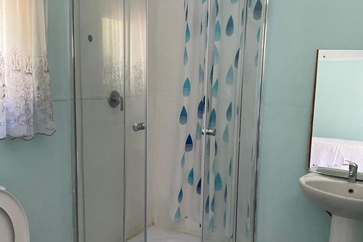 A functional bathroom featuring a corner shower enclosure, pedestal basin, and toilet, with dated finishes and flooring in need of modernization.