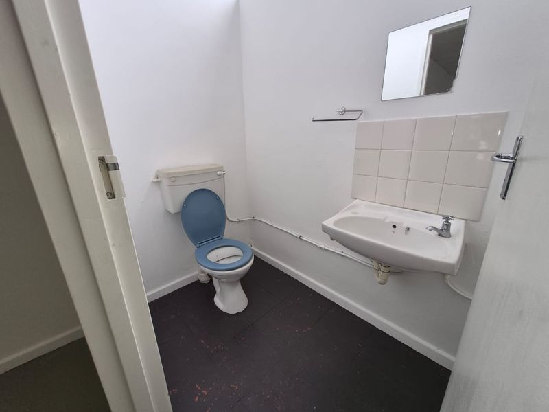 A functional, compact bathroom featuring a toilet, wall-mounted basin with tiled splashback, and basic fixtures, presenting an opportunity for cosmetic updates.